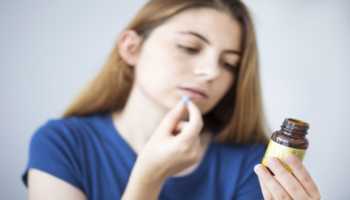 Woman Taking Pill While Reading Bottle