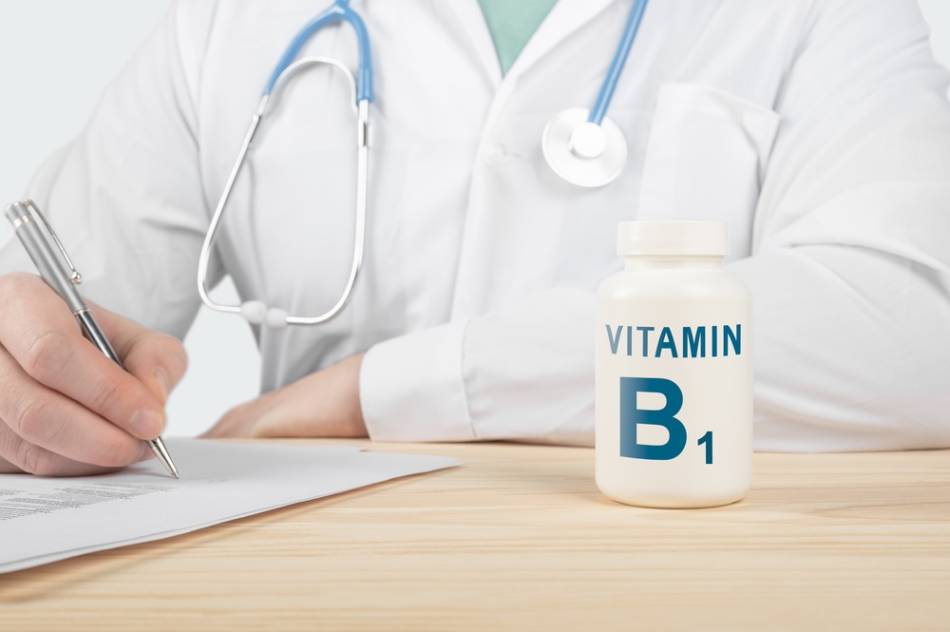 Doctor Sitting on Desk with Vitamin B-1 Bottle