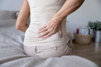 Mature Woman Sitting on Bed Due to Backpain