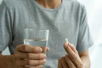 Man in Grey Tee Holding Water and White Supplement