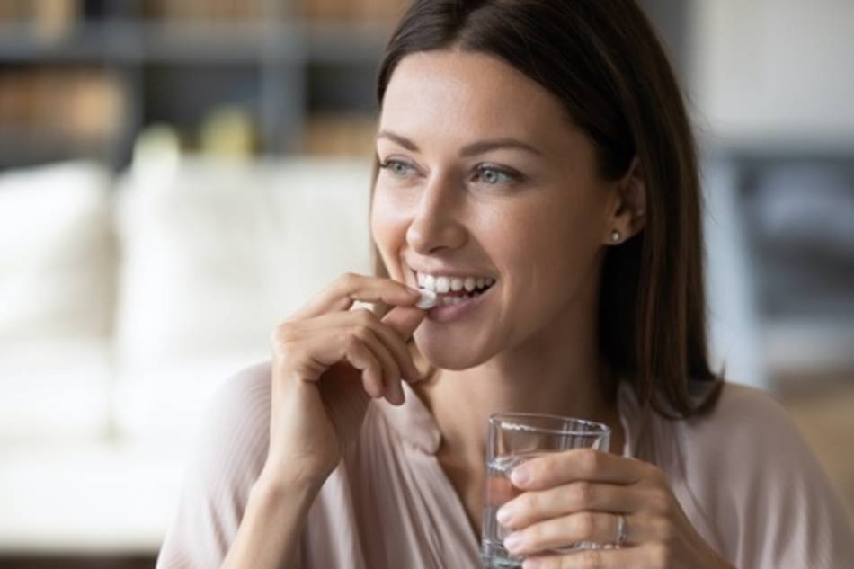 Smiling Woman Taking White Supplement with Glass of Water