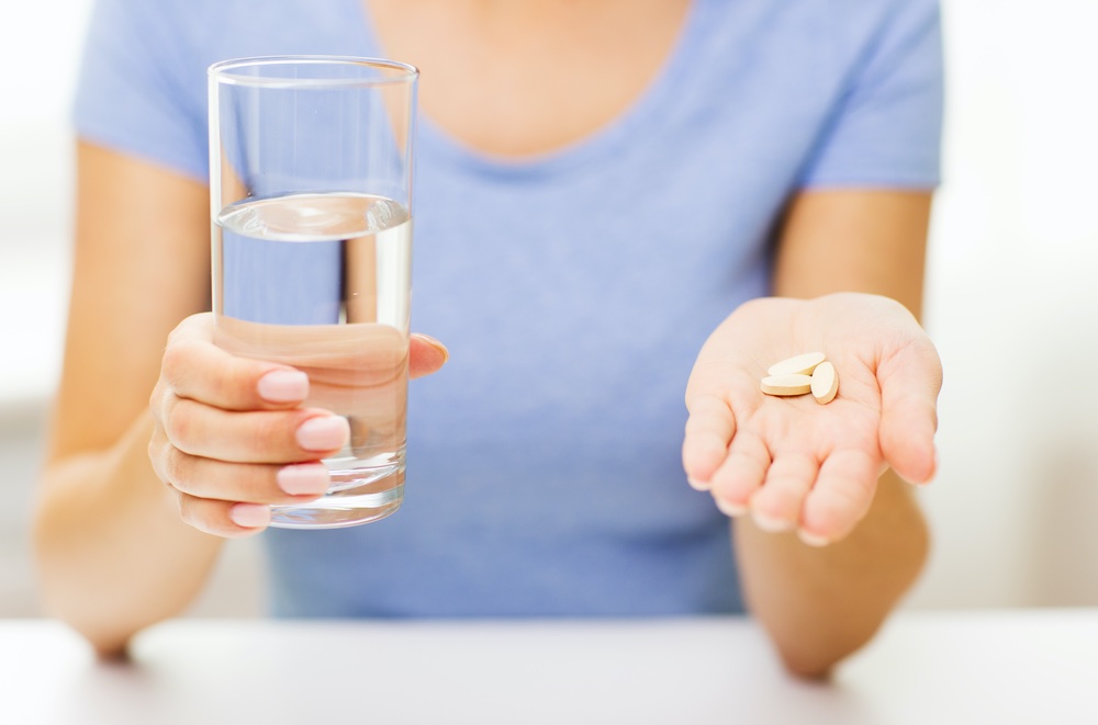 Women Holding Glass in One Hand and Vitamins in the Other