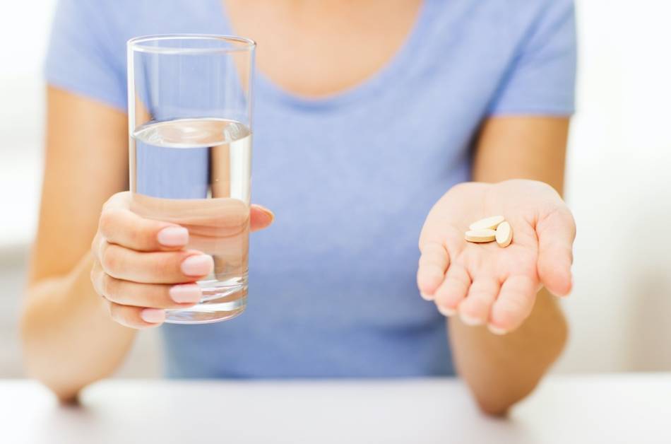 Women Holding Glass in One Hand and Vitamins in the Other