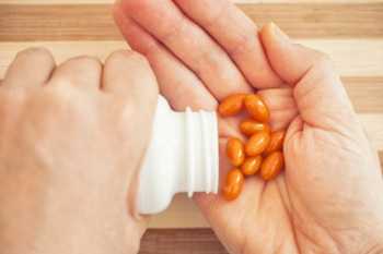 Orange Pills from Supplement Bottle Falling into Hand