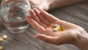 Woman holding various vitamins and supplements in one hand and glass of water in the other