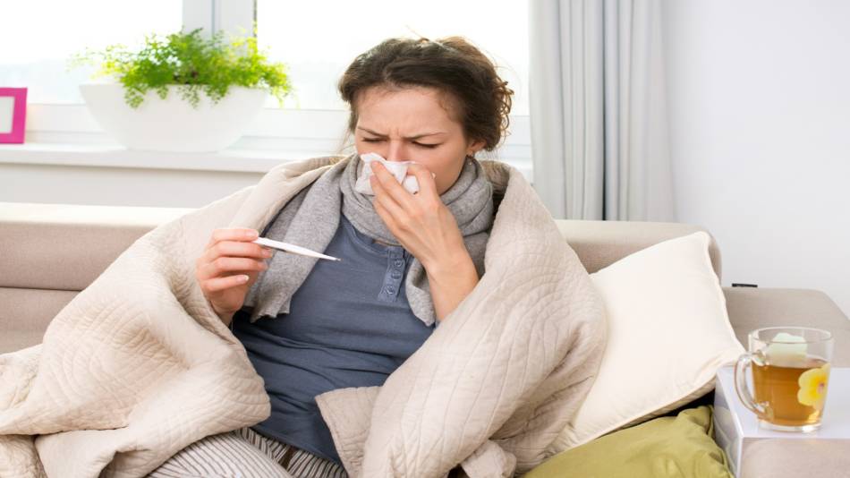 Supplements for Flu -- women with the flu sitting on couch with tissues, thermometer, warm drink