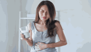 Woman with Stomach Pain Holding Glass of Milk