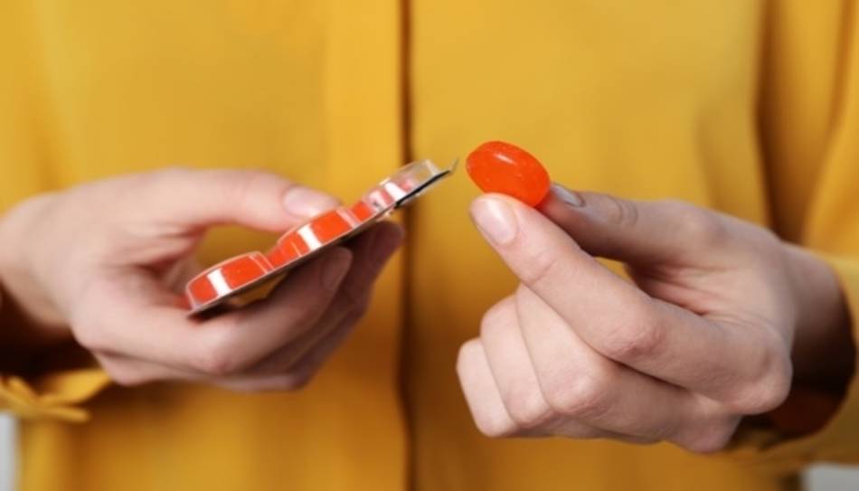 Person in Yellow Holding Blister Pack and Red Lozenge