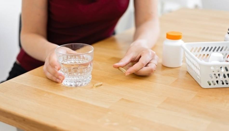 Person with Fish Oil Supplement and Water on Kitchen Counter