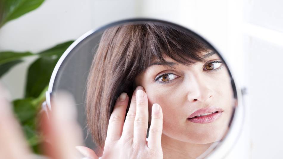 Collagen Supplements for Wrinkles? -- woman looking closely at her face in a mirror