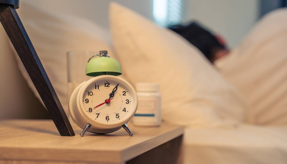 Alarm Clock On Nightstand with Supplement Bottle in Background
