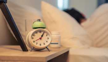 Alarm Clock On Nightstand with Supplement Bottle in Background