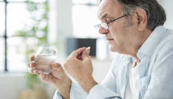 Elderly Man Taking Supplement with Glass of Water