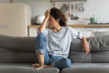 Woman On Couch Holding Head Due to Headache