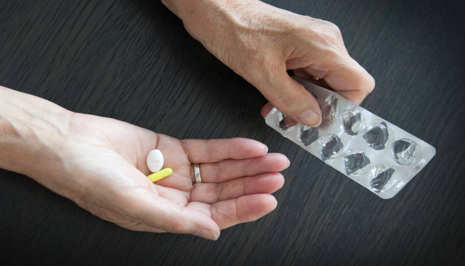 Elderly Individual Taking Two Supplements from Blister Packs