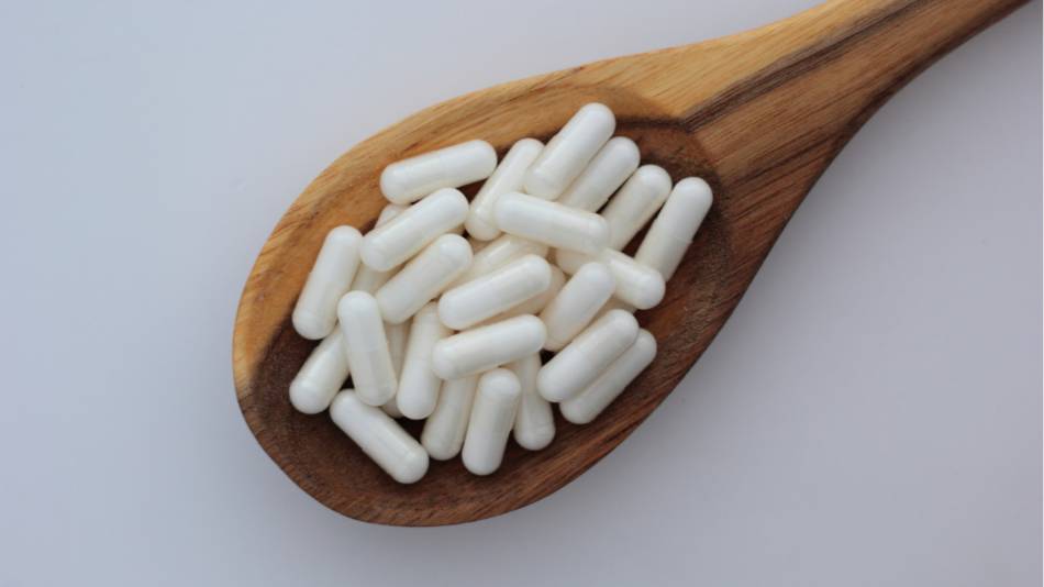 Wooden spoon filled with white inositol capsules