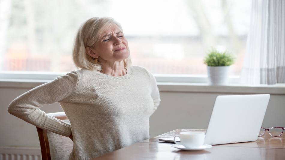 Chuchuhuasi for Inflammation & Back Pain? -- Woman With Back Pain Sitting, at Desk Drinking Tea