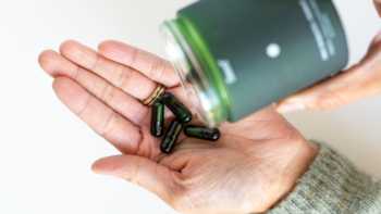 Person pouring Daily Synbiotic capsules from container into other hand