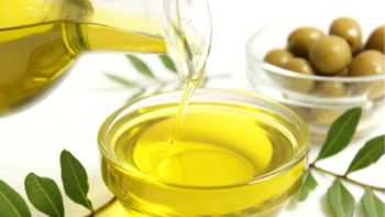 Olive oil being poured into bowl with bowl of olives in the background