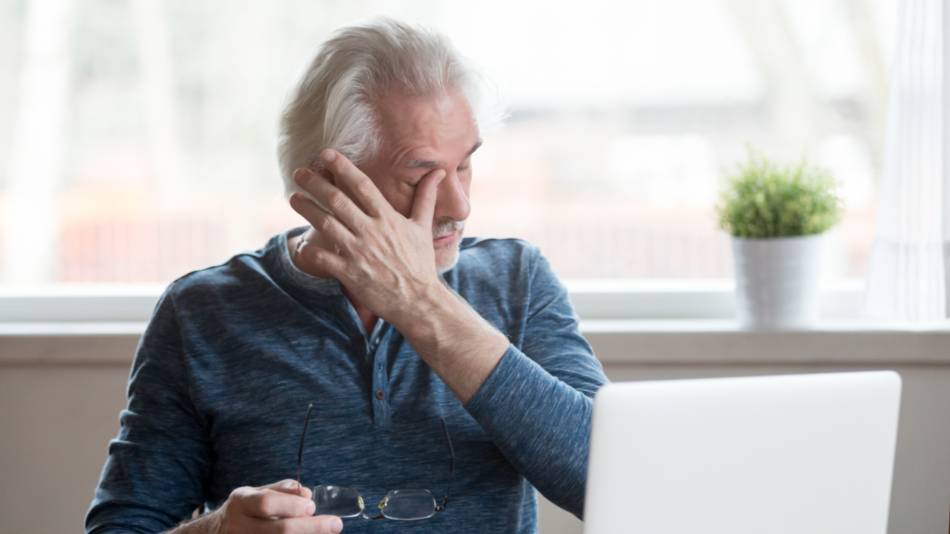 Older man with dry eye rubbing his eyes while holding his glasses