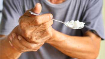 Elderly man with parkinsons holding trembling hand while eating