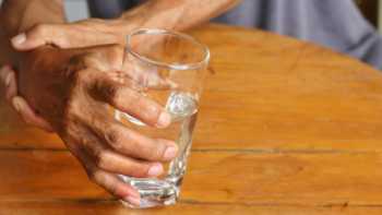 Man with essential tremor holding a cup with his right hand and bracing his wrist with his left hand