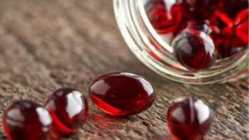 Capsules of astaxanthin being poured onto a wooden table