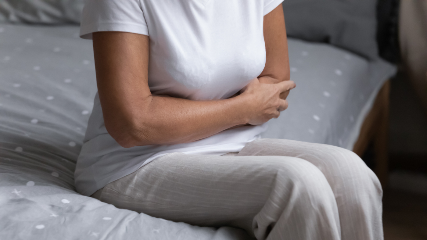 Older woman sitting on her bed and holding her stomach due to gas and bloating