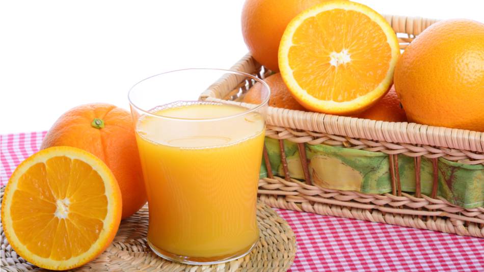 A glass of orange juice sitting on a table and surrounded by sliced and whole oranges