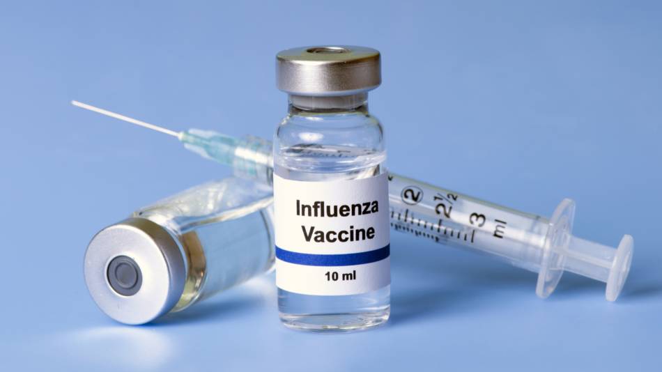 Vial of flu vaccine in front of a syringe and another vial