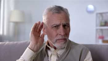 Older man holding his hand up to his ear due to hearing loss