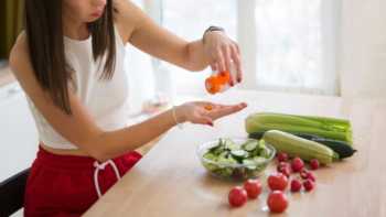 Woman pouring supplements into her hand while sitting in front of a table on which vegetables are placed