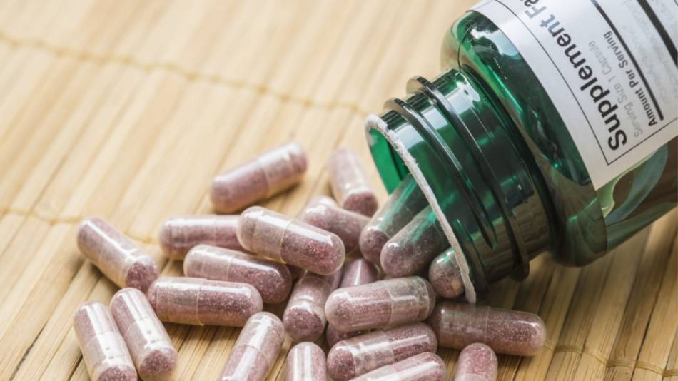 Herbal capsules being poured out of supplement container onto table