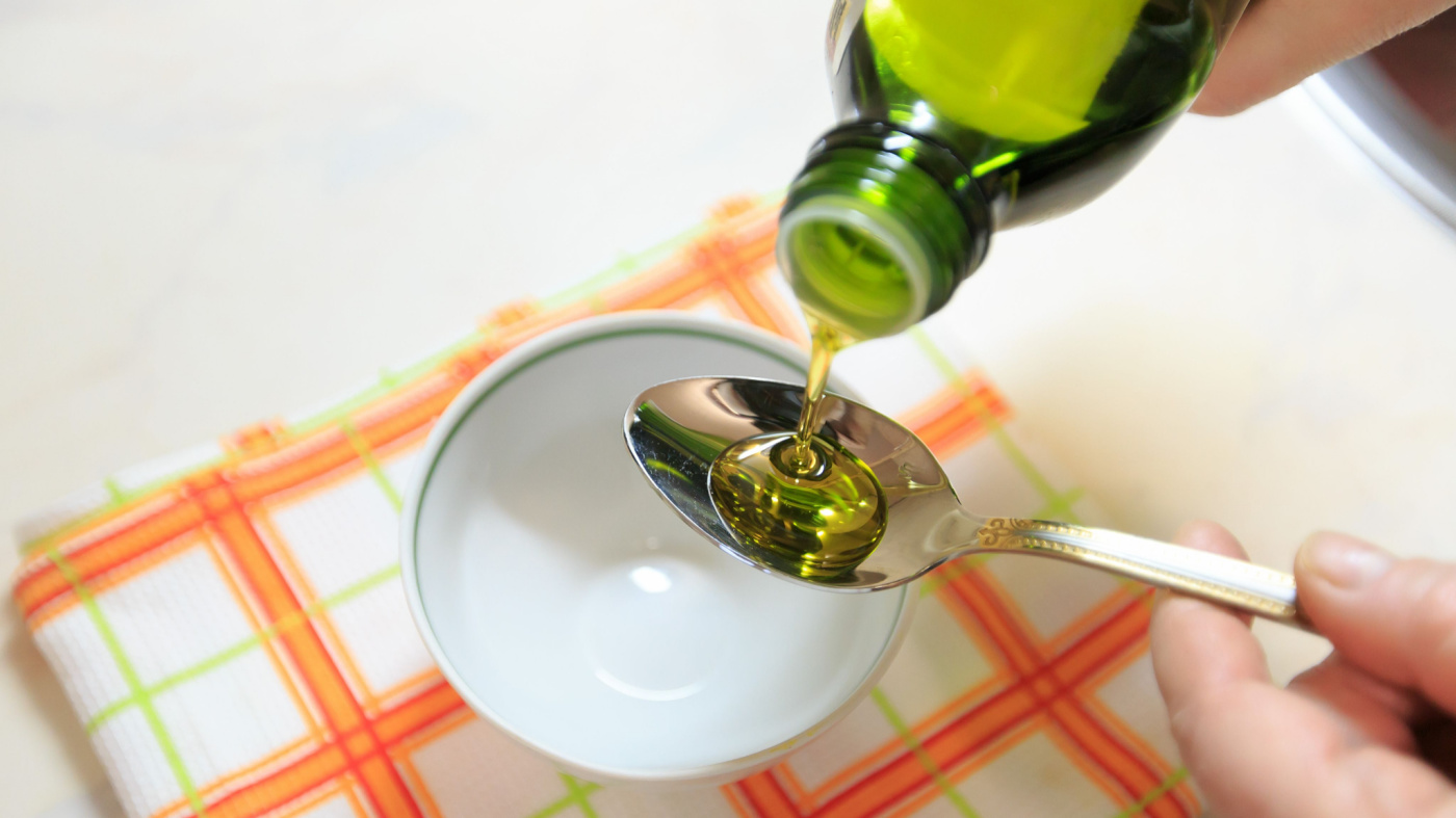 Olive oil being poured into a spoon being held over a bowl
