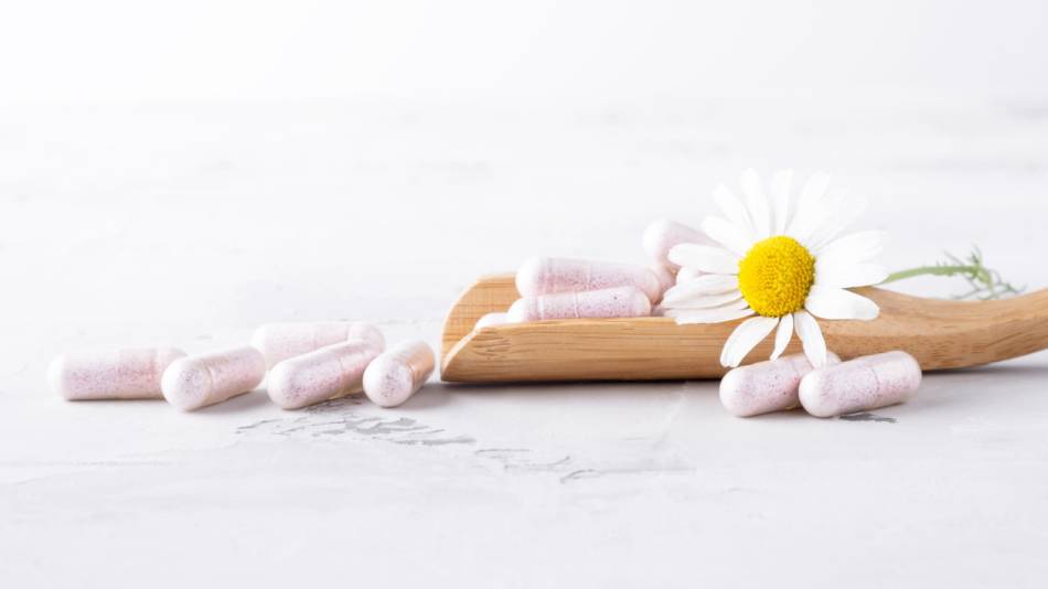 Apigenin capsules on wooden spoon along with a chamomile flower