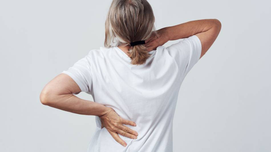 Woman rubbing her neck and lower back to try to relieve overall aches and stiffness