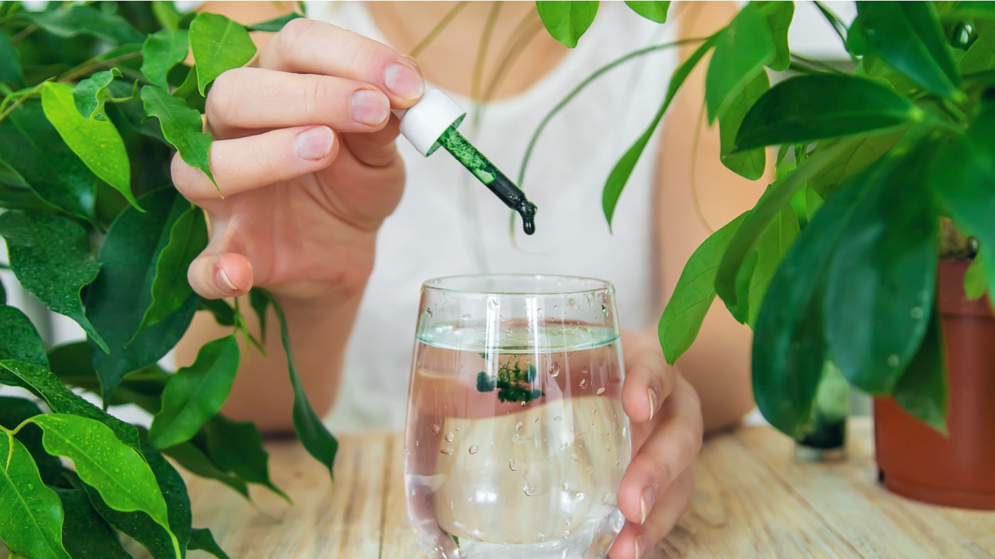 Woman adding drops of liquid chlorophyll to glass of water