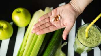 Woman holding detox supplements in the palm of her hand over various fruits and vegetables on a table