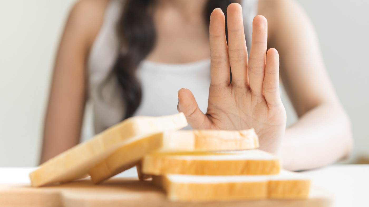 Woman holding her hand in front of a slice of bread to signify a gluten free diet