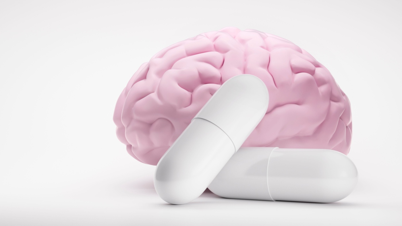 Two white pills in front of a brain