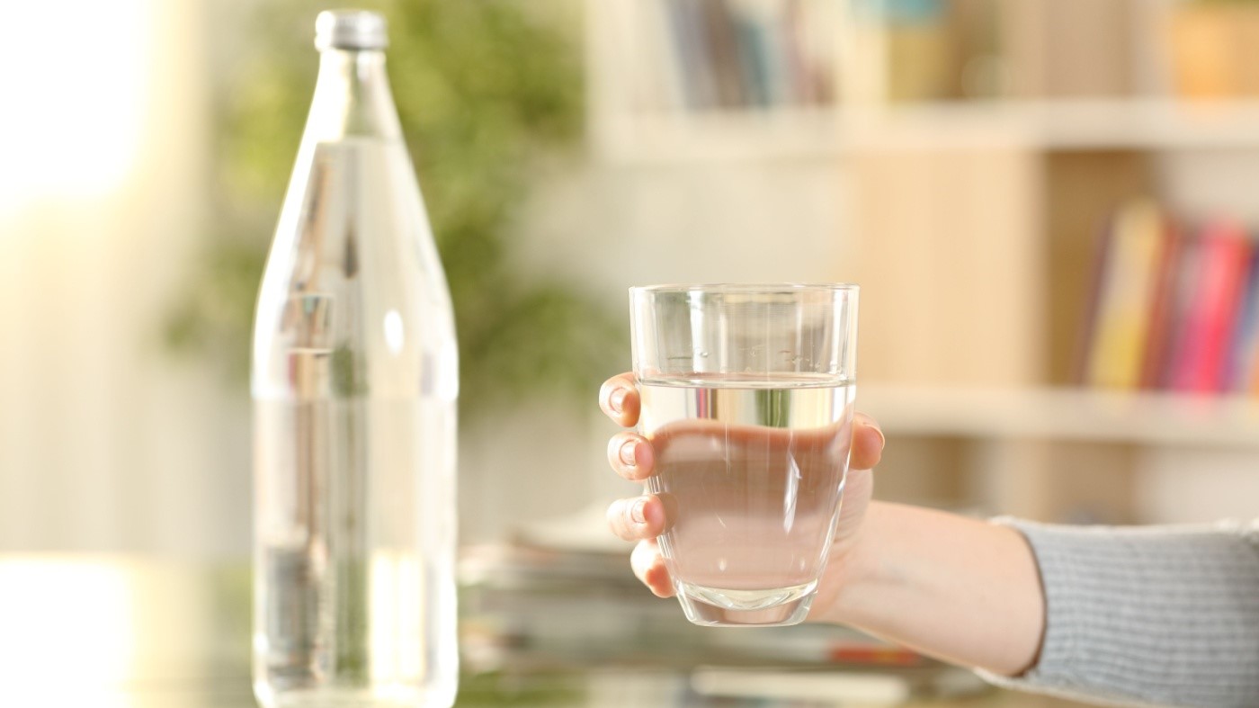 Woman holding glass of water next to bottle of water