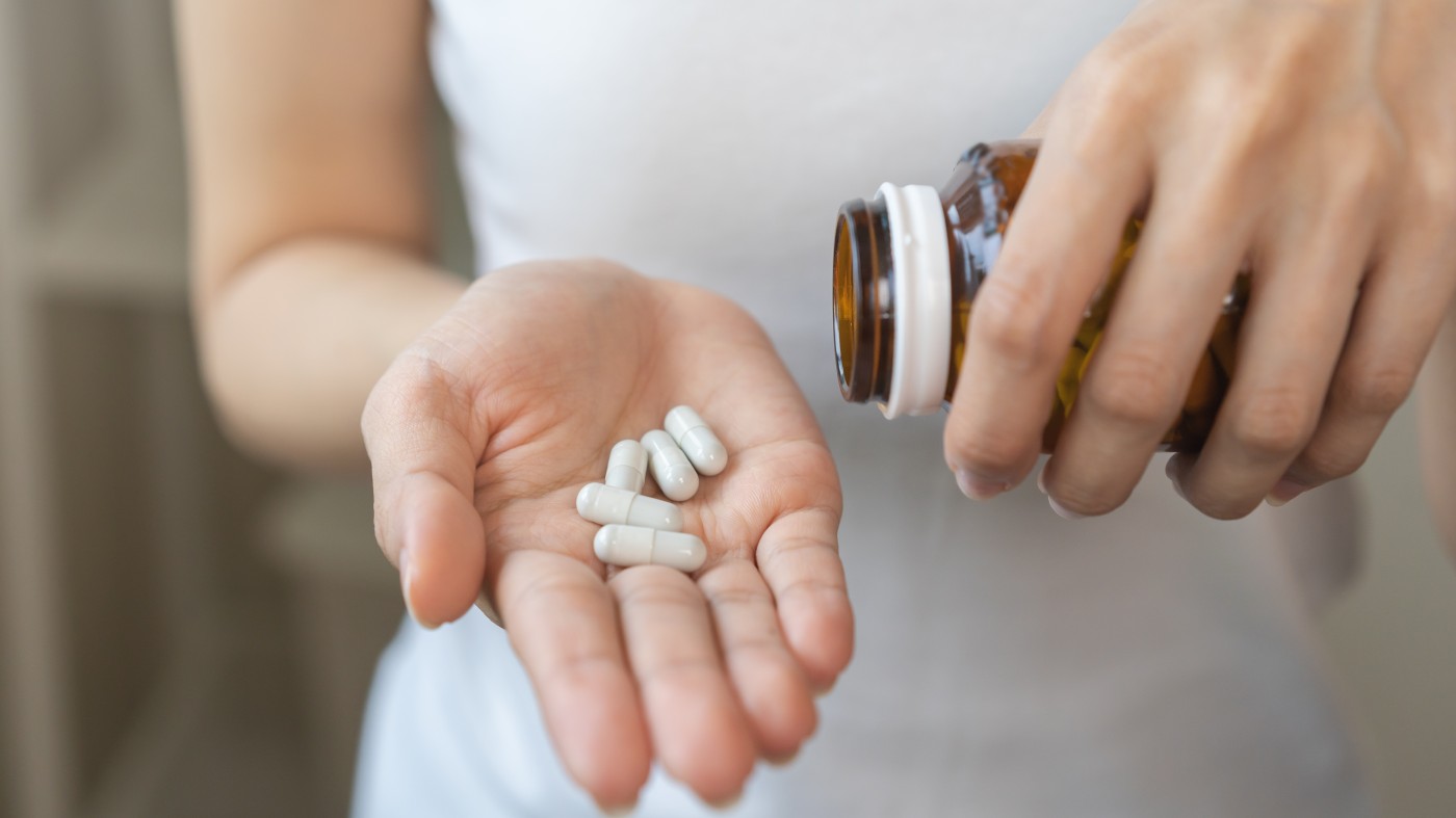 woman pouring white capsules from a pill bottle into her hand
