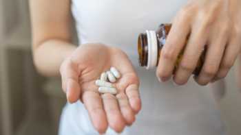 woman pouring white capsules from a pill bottle into her hand