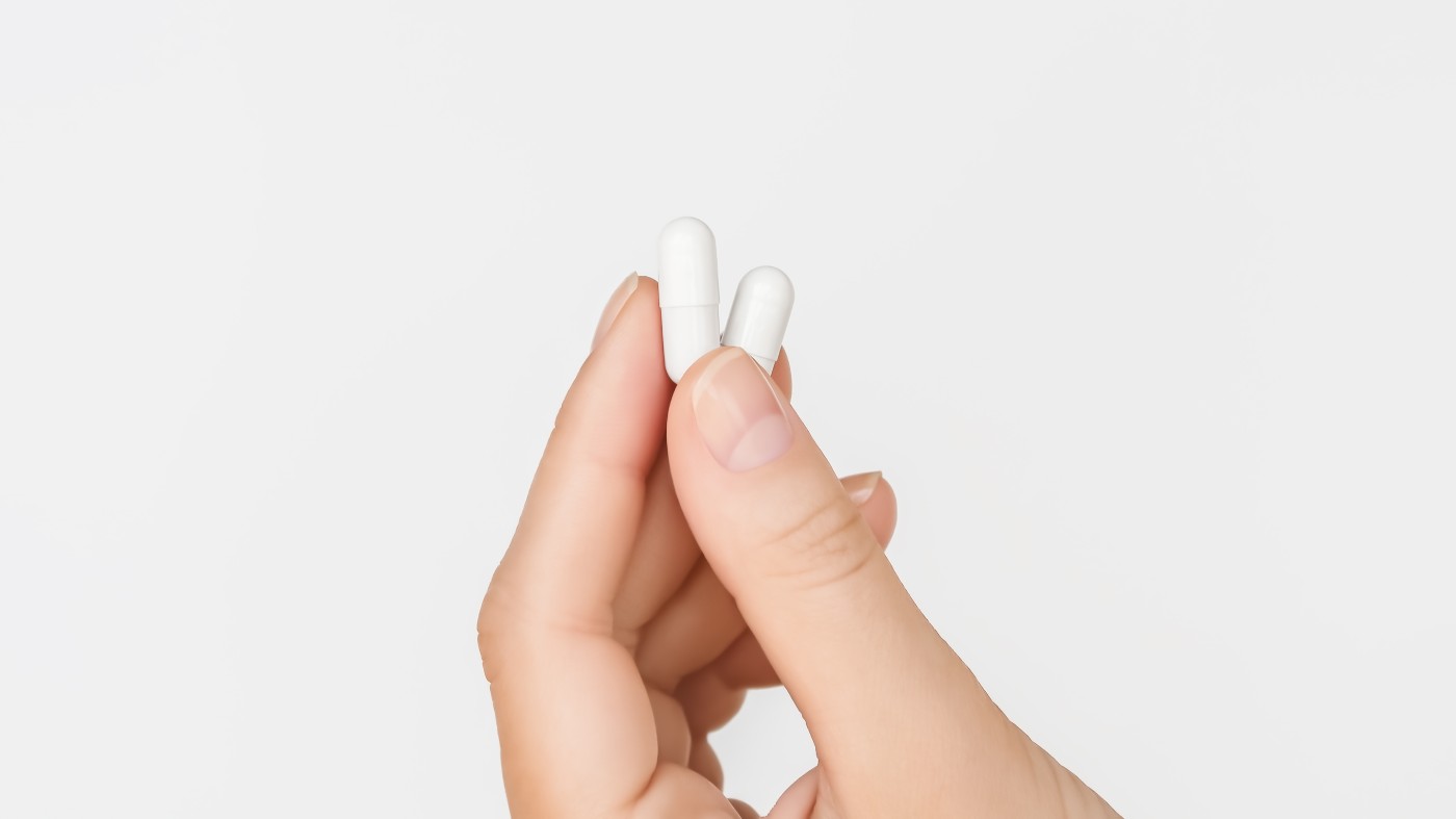 Woman holding two capsules of magnesium l-threonate