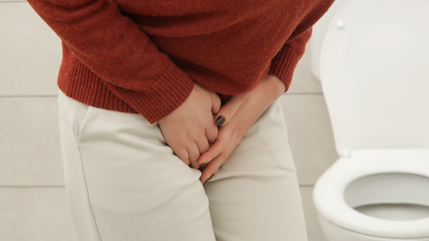 Woman standing in bathroom holding her abdomen due to bladder pain caused by uti
